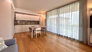 A modern living room with a dining area, wooden flooring, a sofa, a TV, and large windows with curtains. - Large, bright and modern flat with an incredible view on lake Garda in Malcesine (Malcesine)