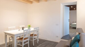 A dining area with a white table and chairs, a small plant on the table, and a doorway leading to another room.