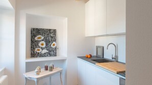 A compact kitchen with white cabinets, a wooden countertop, a sink, and a small table with jars.