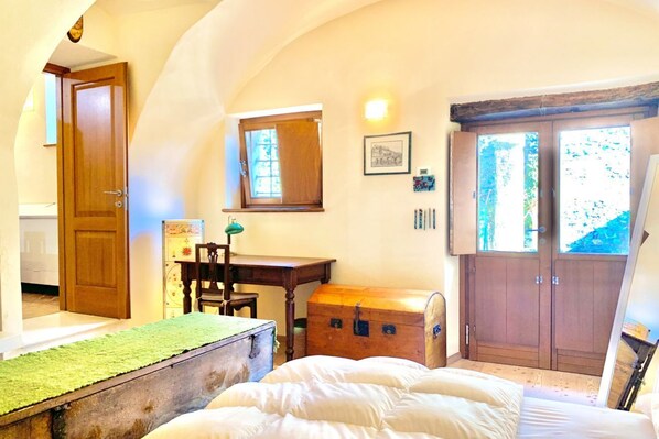 Un dormitorio con cama, escritorio, silla, un cofre de madera y un armario.