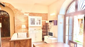 Quarto aconchegante com parede de tijolos, um banco de madeira, armário branco, televisão e uma grande janela.