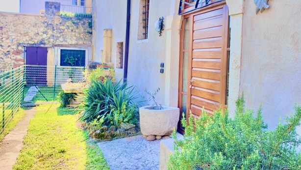 Um pátio com parede de pedra, porta de madeira e pequeno jardim com plantas e um vaso de pedra.