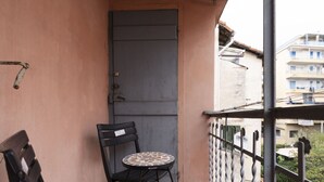 Un balcon avec une porte, une petite table ronde et deux chaises noires.
