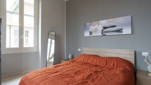 Une chambre à coucher comprenant un lit, une table de chevet, une commode, un miroir et une fenêtre avec des stores.