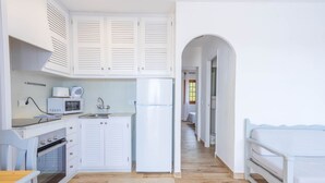 Une cuisine de taille réduite, avec des meubles blancs, un four à micro-ondes, un évier et un réfrigérateur.