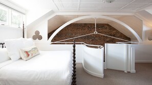 A bedroom with a white bed, a hanging chair, a brick wall, and a white ceiling.