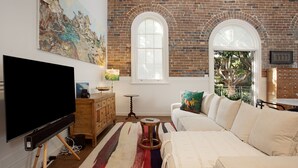 Un salon avec un téléviseur, des meubles en bois, un tapis coloré et un mur en briques agrémenté de fenêtres en arc de cercle.