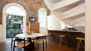 Une cuisine moderne avec un mur en briques, une table de salle à manger ronde entourée de chaises et un coin bar avec des tabourets.