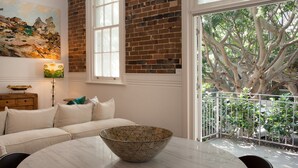 Une pièce avec un canapé blanc, une table en marbre, un grand tableau et une vue sur un arbre par la fenêtre.