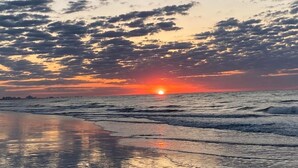 A beach at sunset with the sun low on the horizon, reflecting on the water. - Oceanfront - Couples Modern Miami Inspired (Myrtle Beach)