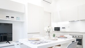 Una cocina moderna con armarios blancos, una mesa de comedor para cuatro personas y un televisor de pantalla plana sobre un soporte blanco.