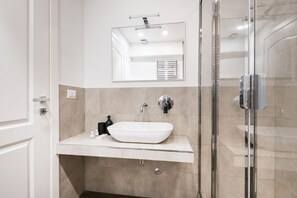 Ein modernes Badezimmer mit einem weißen Waschtisch, einem großen Spiegel und einer Duschkabine aus Glas.