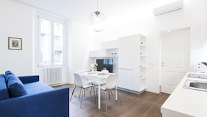 Un apartamento moderno y luminoso con comedor, kitchenette y un sofá azul.