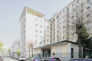 Un immeuble résidentiel à plusieurs étages, avec une rangée de voitures garées devant.