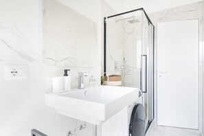Une salle de bain moderne avec un lavabo blanc, une douche en verre et des murs en marbre.