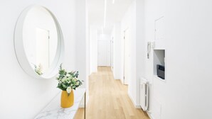 A bright, modern hallway with a wooden floor, white walls, and a large round mirror. A yellow vase with flowers is placed on a marble countertop. - Easylife - Spectacular flat in Citta Studi (Milano)