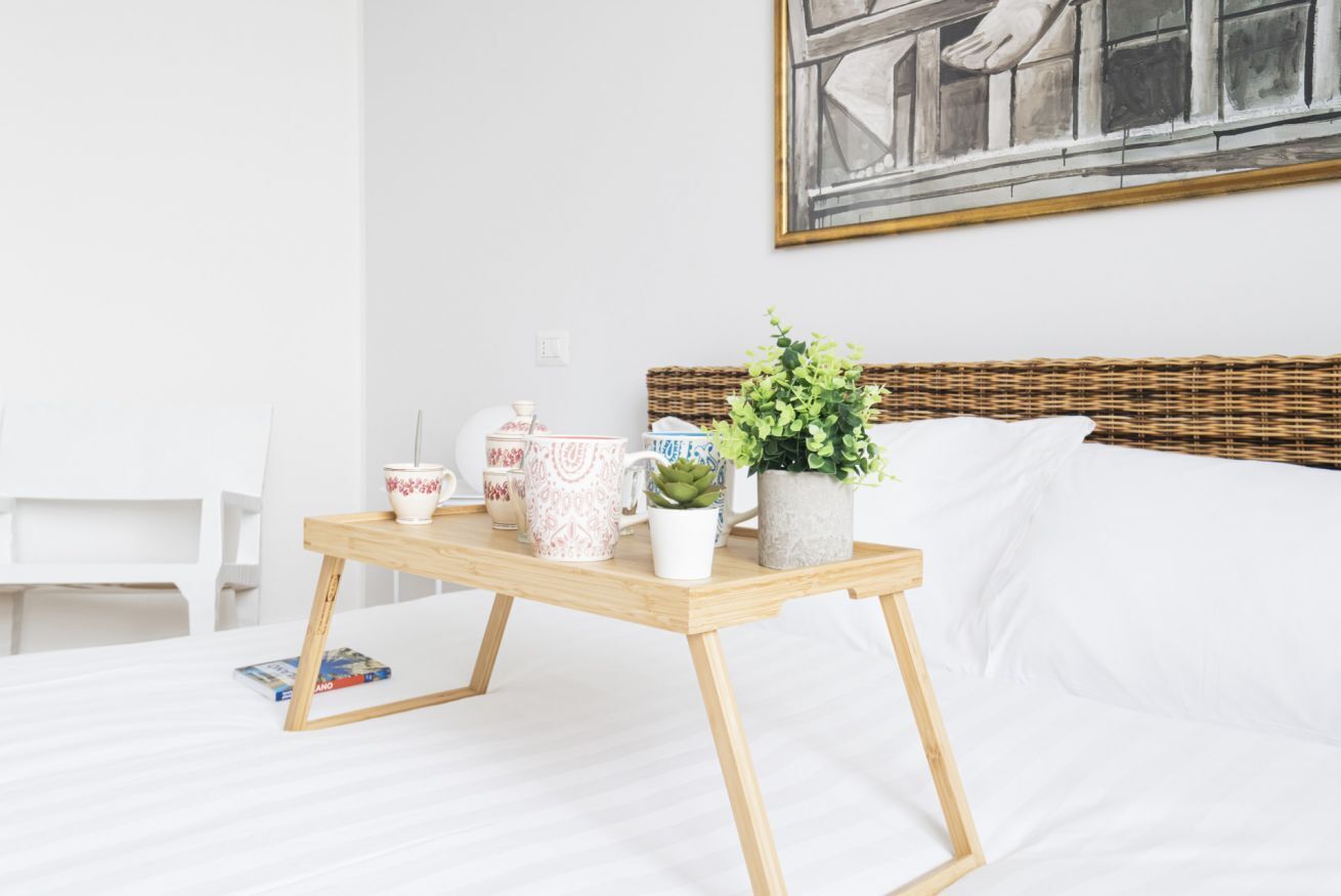 A neatly arranged bedroom with a bed, a bedside table with decorative items, a white chair, and a painting on the wall.