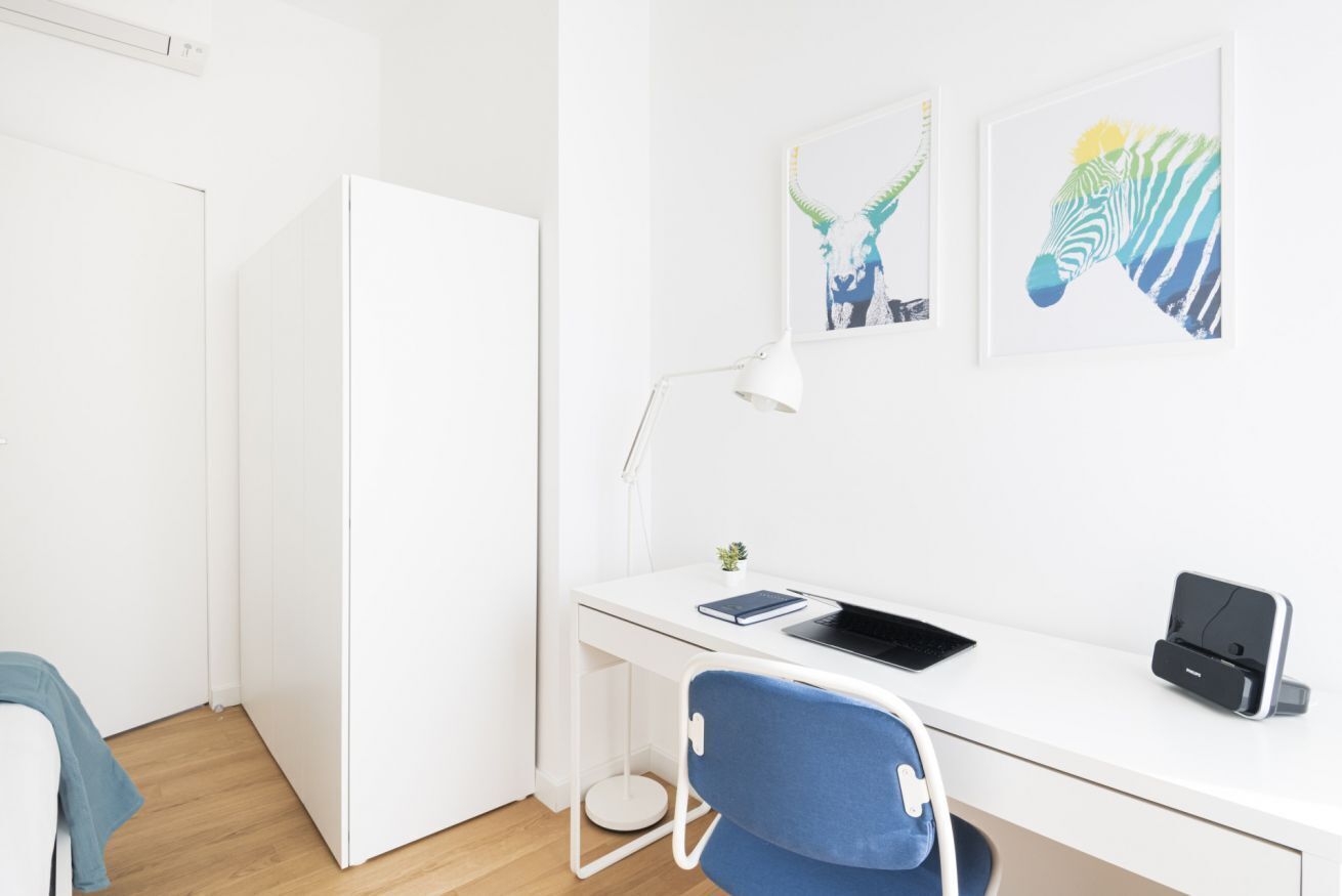 Una habitación moderna y minimalista con un escritorio blanco, una silla azul, un armario blanco y dos cuadros con estampados de cebra en la pared.