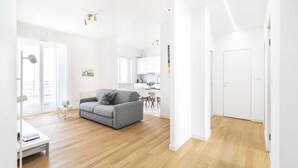 A modern living room with a grey sofa, wooden flooring, and a white dining area. - Easylife - Spectacular flat in Citta Studi (Milano)