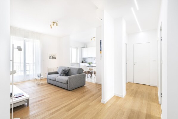Un salon moderne avec un canapé gris, un parquet en bois et un coin repas blanc.