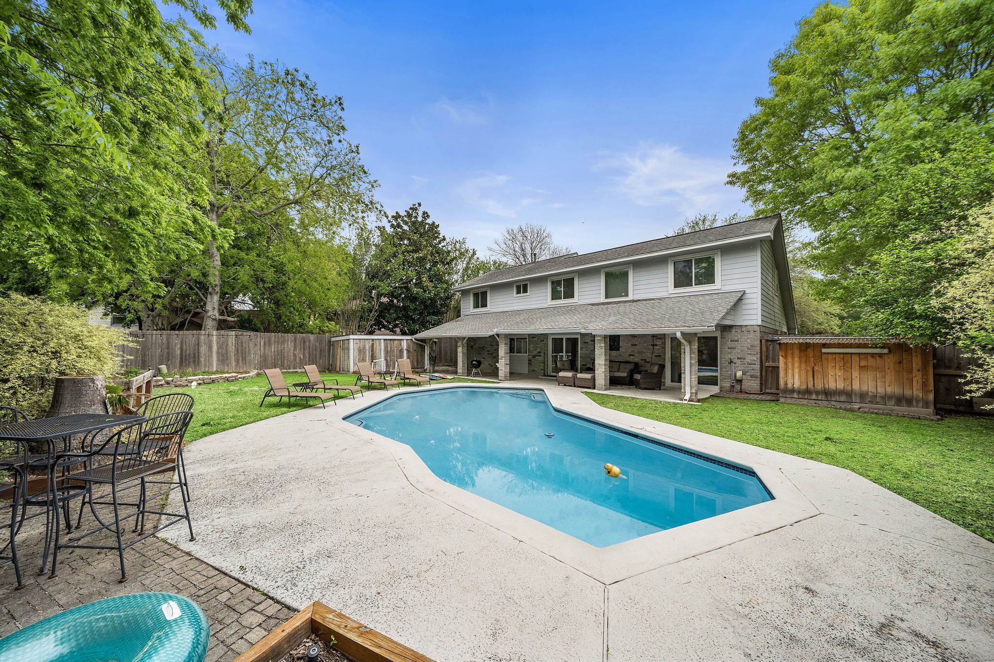 Un jardin avec une piscine, une terrasse avec des chaises et une clôture en bois.