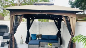 Een terras buiten met een overdekte zithoek, een barbecue en een lichtslingering.
