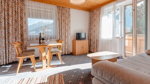 Ein gemütliches Zimmer mit Holzbalkendecke, einem Esstisch mit Stühlen, einer Couch, einem Fernseher und einer Glastür, die zu einem Außenbereich führt.
