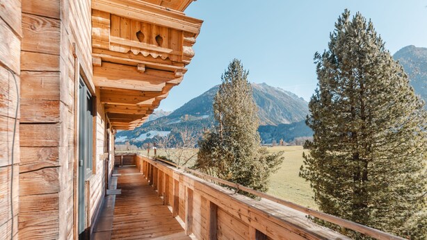 Un balcon en bois offrant une vue sur les montagnes et les arbres.