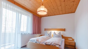 Une chambre avec un plafond en bois, un lit avec deux oreillers, une table de chevet et une fenêtre avec des rideaux légers.
