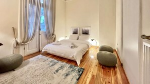 A bedroom with a bed, two bedside lamps, a window with curtains, a patterned rug, and a radiator. - Magnolia: Spacious neoclassical apartment (Thessaloniki)