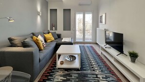 A modern living room with a grey sofa, a white coffee table, a flat-screen TV, and a patterned rug. - Liberty: Vibrant family apartment (Thessaloniki)