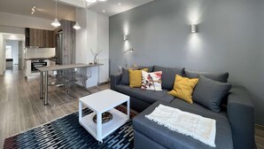 A modern living room with a grey sofa, a white coffee table, and a dining area with a kitchen in the background. - Liberty: Vibrant family apartment (Thessaloniki)