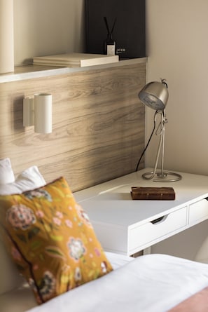 Une chambre moderne avec un bureau blanc, une lampe, un coussin décoratif et une petite étagère sur laquelle se trouvent une bouteille et une boîte.