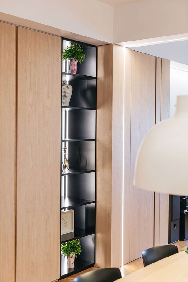 Un interior moderno con un panel de madera, una estantería negra con plantas y una zona de comedor con mesa y sillas.