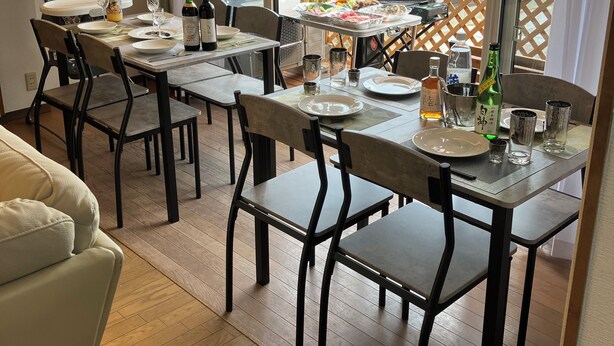 A dining area with a table set for four, a sofa, and a view of a balcony with a wooden fence. - Bigstone Terrace Suite Tsutsumimachi (Aomori)