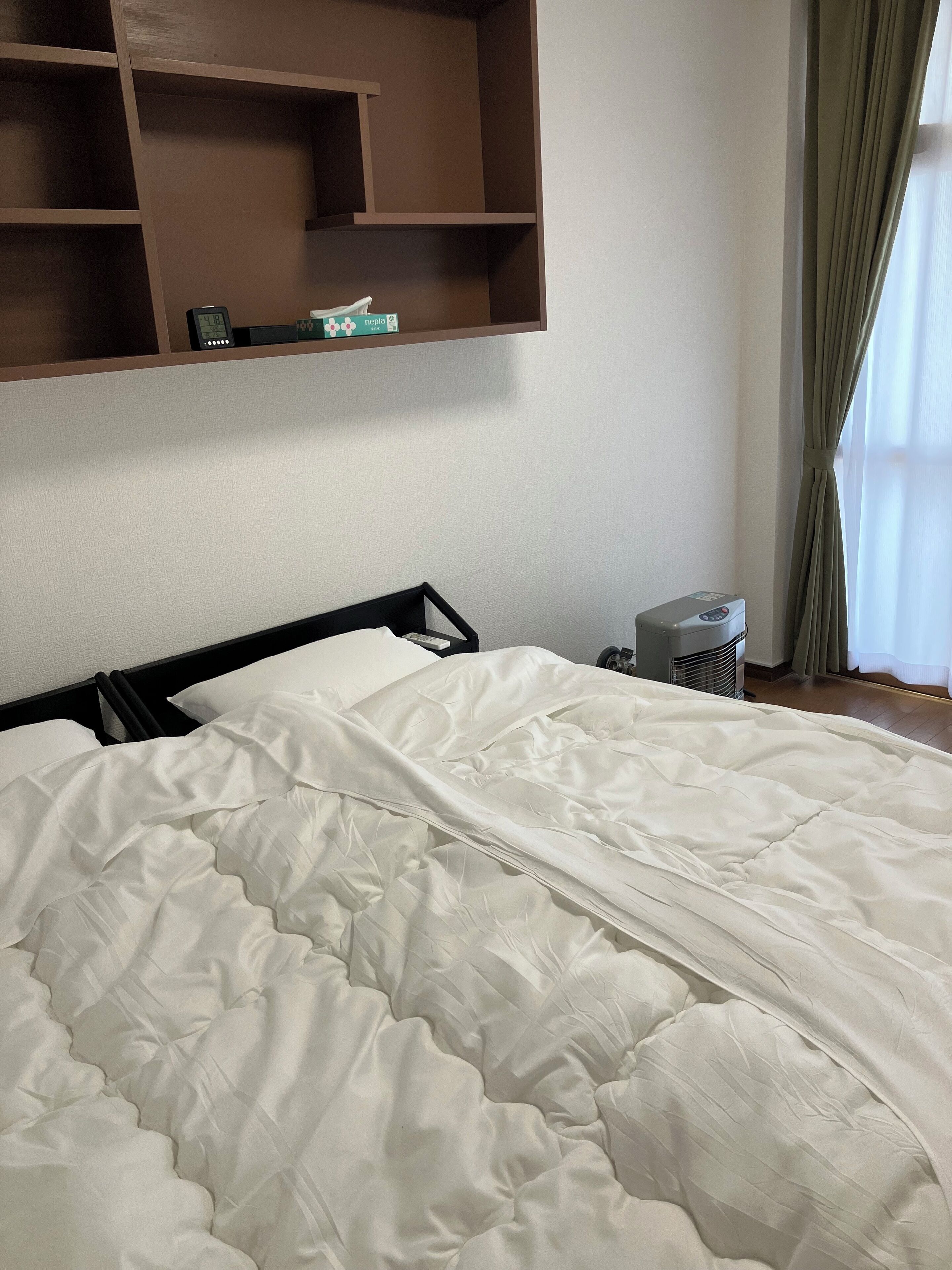 A neatly made bed with a white duvet, a bedside table with a lamp, and a shelf above the bed.