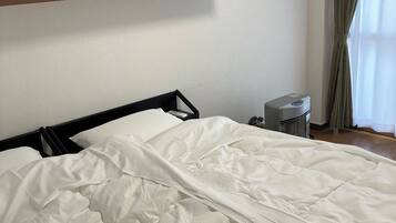 A neatly made bed with a white duvet, a bedside table with a lamp, and a shelf above the bed.