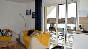 A modern living room with a sofa, a small table, and a balcony with chairs. - Entre Plage et Ports : Le 49 - Avec Balcon (Courseulles-sur-Mer)