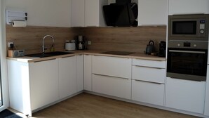 A modern kitchen with white cabinets, a wooden countertop, a built-in microwave, and a kettle. - Entre Plage et Ports : Le 49 - Avec Balcon (Courseulles-sur-Mer)