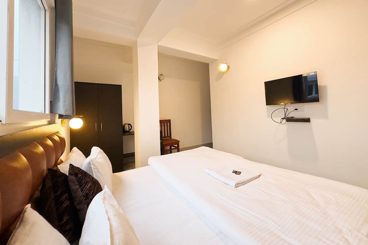 Une chambre d’hôtel avec un lit, un téléviseur fixé au mur et une fenêtre avec des rideaux.