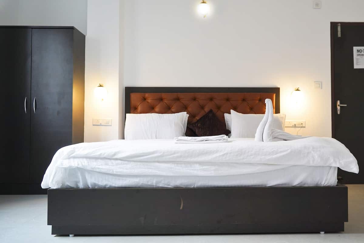 Un lit bien fait, avec du linge de lit blanc et des oreillers, une tête de lit sombre et un luminaire fixé au mur.