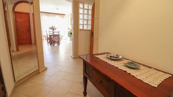A hallway with a wooden table, a lace table runner, and a door leading to another room.