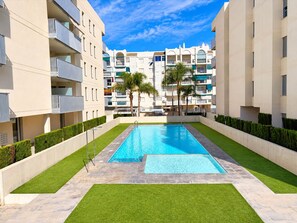 Une piscine entourée de haies soigneusement taillées et d’une pelouse bien entretenue, avec des immeubles à plusieurs étages en arrière-plan.