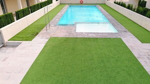 Une piscine rectangulaire entourée d’une zone pavée et d’une pelouse artificielle.