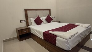 Una cama bien hecha con cabecera de madera, dos mesitas de noche y una colcha estampada en rojo y blanco.