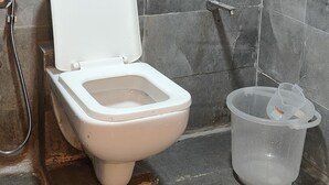 Un baño con inodoro, ducha y un recipiente de plástico en el suelo.