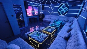 A modern lounge area with a large flat-screen TV, neon lighting, and a plush seating arrangement.