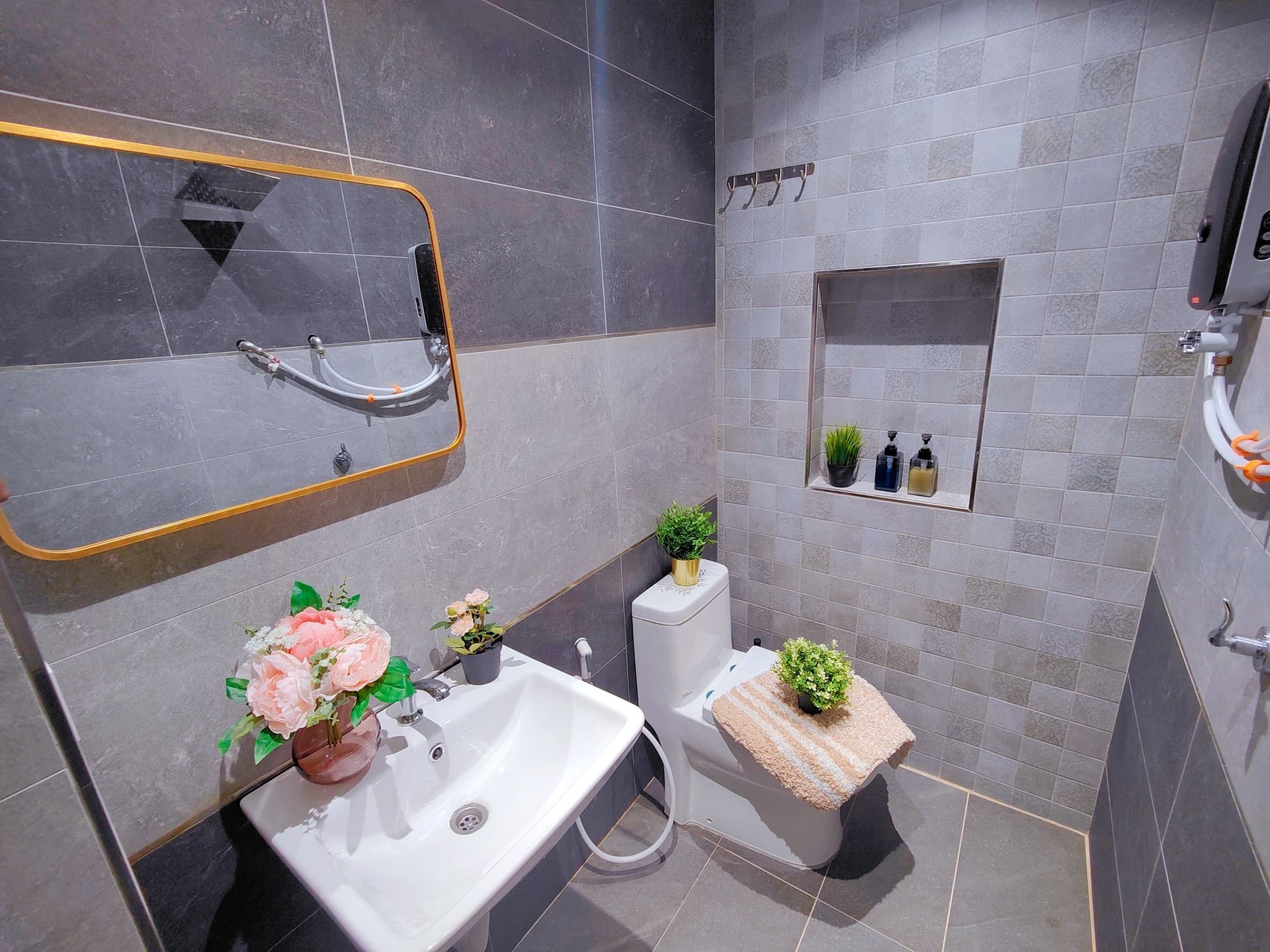A modern bathroom with a white sink, a mirror with a gold frame, a toilet with a small shelf, and a shower area.