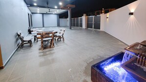 A spacious outdoor patio with a round table and chairs, a ceiling fan, and a water feature.