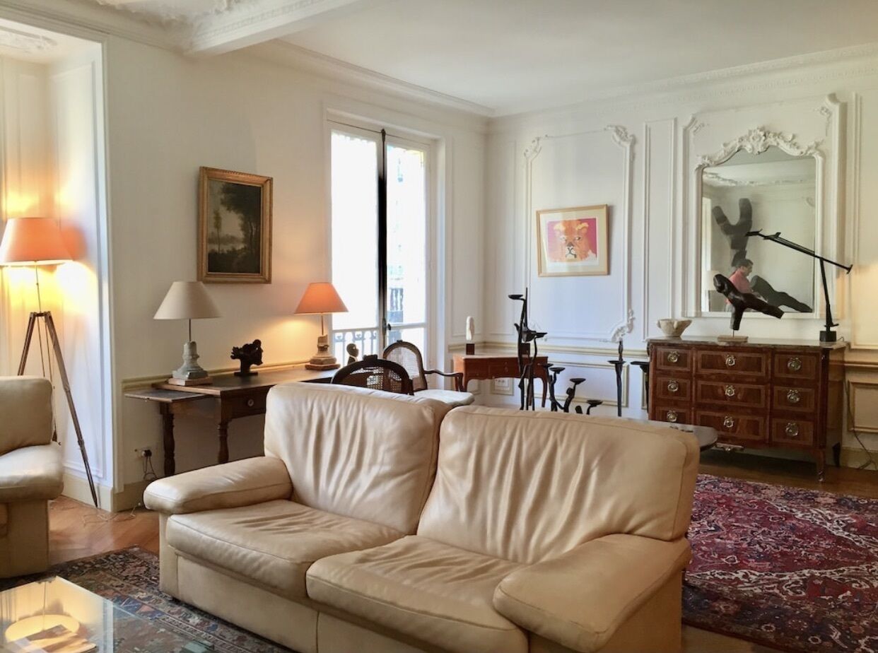 Een woonkamer met een beige bank, een houten bureau, een lamp en een spiegel.